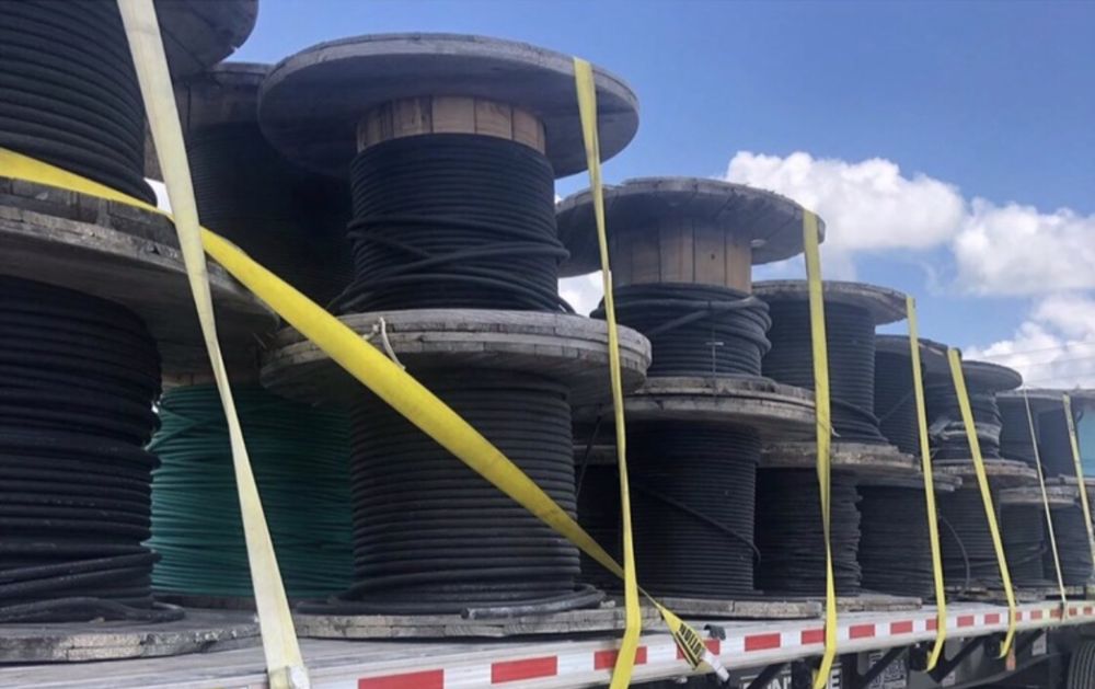 Flatbed trailer loaded with wooden cable reels secured with yellow straps